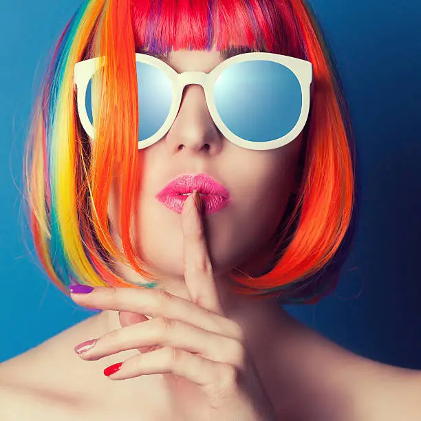 Photo of beautiful woman wearing colorful wig and white sunglasses agains