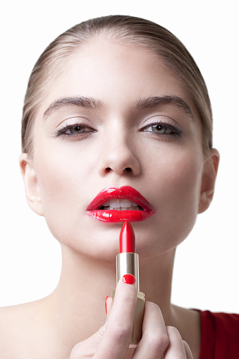 A stunning blonde fashion model in red lipstick holds a tube of red lipstick near her mouth