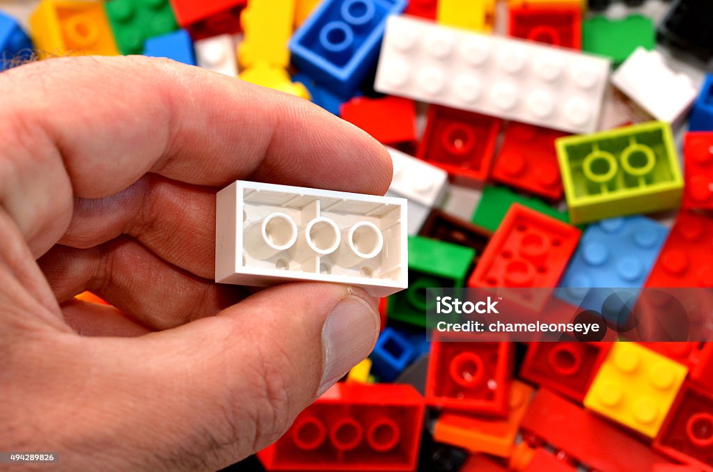 Building blocks Mans hand holds a red toy block against mix of building blocks background. concept photo of imagination, creativity, planning and ideas 2015 Stock Photo
