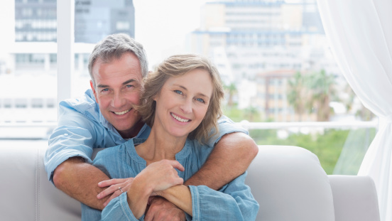 Content man hugging his wife on the couch smiling at camera at home in the living room