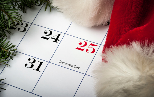 Santa hat laying on a calendar next to December 25th Christmas with evergreens