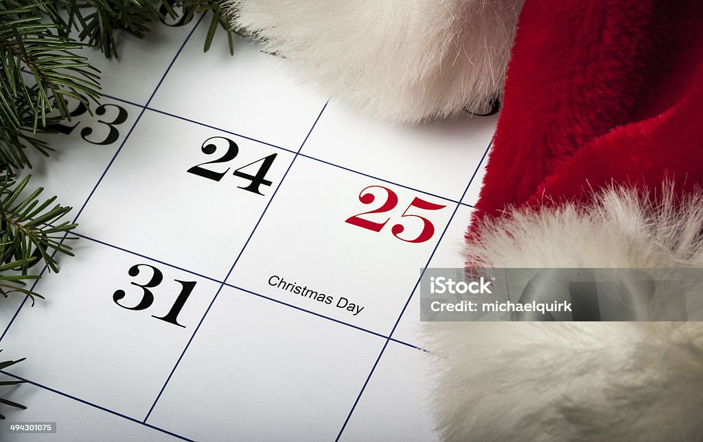 Santa hat laying on a Christmas calendar Santa hat laying on a calendar next to December 25th Christmas with evergreens Christmas Stock Photo