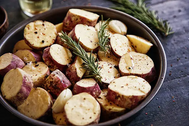 Raw sweet potato with rosemary, pepper and olive oil prepared for oven roasting