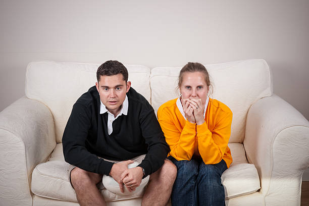 Pair Of Rugby Fans On Rival Team Watching Tense Match A portrait of a caucasian couple supporting opposing rugby teams  watching a tense match. nail biting stock pictures, royalty-free photos & images