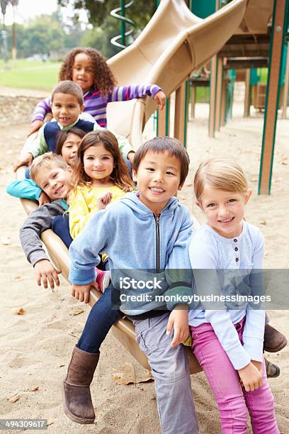 Group Of Young Children Sitting On Slide In Playground Stock Photo - Download Image Now