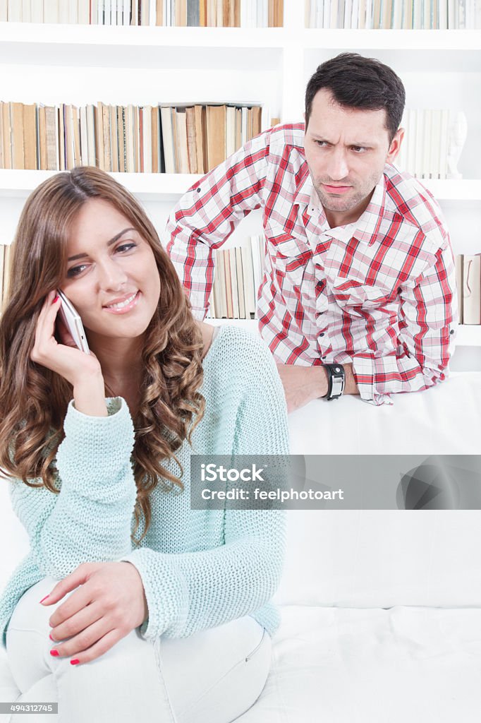 jealous worried man peering over the shoulder of his girlfriend jealous worried man peering over the shoulder of his girlfriend while she is talking on the phone smiling Adult Stock Photo