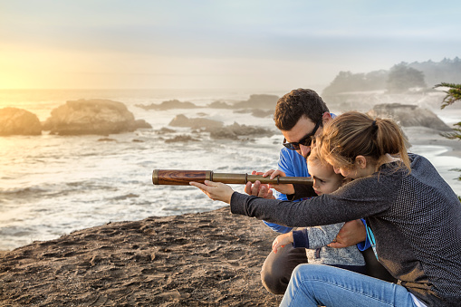 Family with spyglass looking toward ocean at sunset. Concept for discovery or looking toward future.