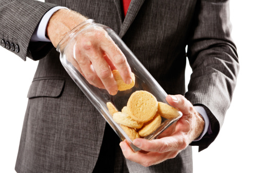 A businessman's hand fishes cookies out of a glass jar. Sweet tooth or metaphor for white-collar crime.