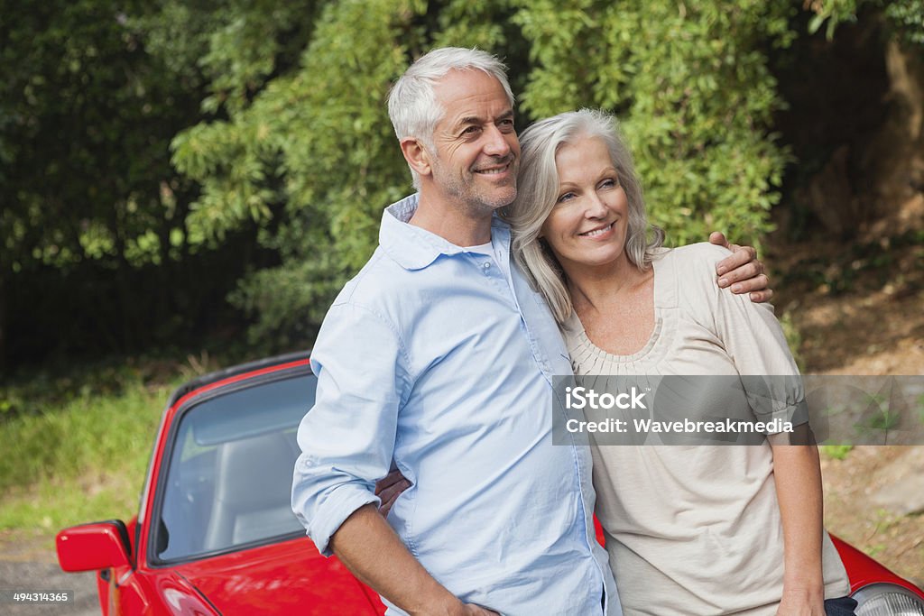 Happy mature couple posing by their red convertible Happy mature couple posing by their red convertible on bright day 50-54 Years Stock Photo