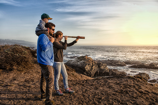 Family with spyglass looking toward ocean at sunset. Concept for discovery or looking toward future.