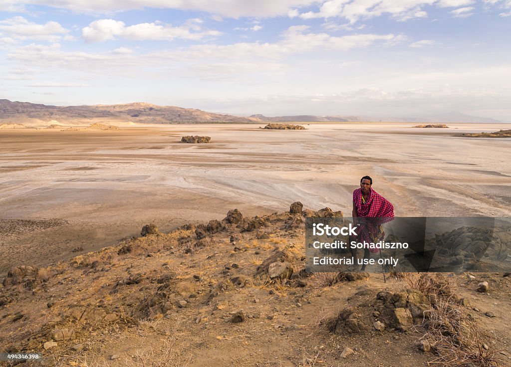 Maasai in Arusha Arusha Region, Tanzania - October 16, 2015: Maasai warrior wearing traditional red clothes walks in the dried part of Lake Natron in the North of Tanzania, Africa, in the early morning. Ol Doinyo Lengai Stock Photo