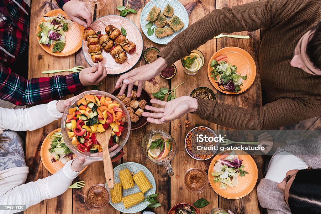 Friends having dinner. Top view of four people having dinner together while sitting at the rustic wooden table Sharing Stock Photo