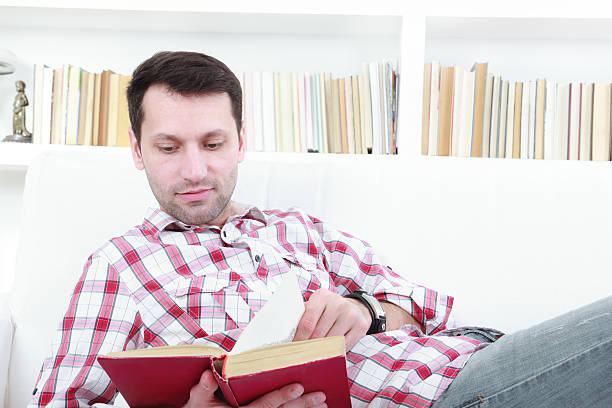 istock young casual man reading a book relaxing on sofa 494349395