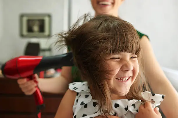 sweet little girl at harsalon drying hair and laughing.hairdresser with hairdryer working.