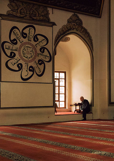 Man Praying in Ulu Cami, Bursa, Turkey Bursa, Turkey - October 24, 2015: Lonely, senior, local man reading quran in the window of Ulu Cami. Bursa Grand Mosque or Ulu Cami was built in the Seljuk style, it was ordered by the Ottoman Sultan Bayezid I and built between 1396 and 1399. Ulu Cami is the largest mosque in Bursa and a landmark of early Ottoman architecture which used many elements from the Seljuk architecture. ulu camii stock pictures, royalty-free photos & images