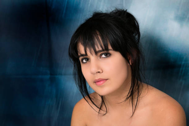 Young woman with black hair and health skin.  Landscape photo.  Dark blue with light blue background. Woman is looking at the camera
