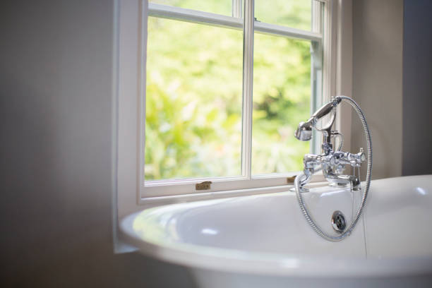 Pure white bathtub with water near window. Bathroom with big window. Mountain view