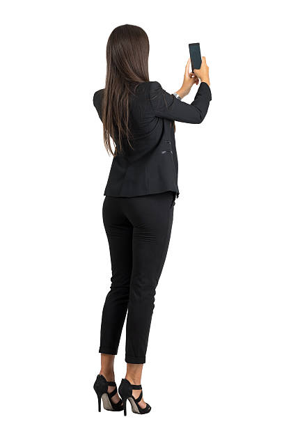Rear view of woman in suit taking photo with cellphone stock photo