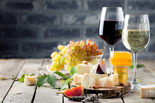 Grape, cheese, figs and honey with a glasses of red and white wine on a stone and wood background