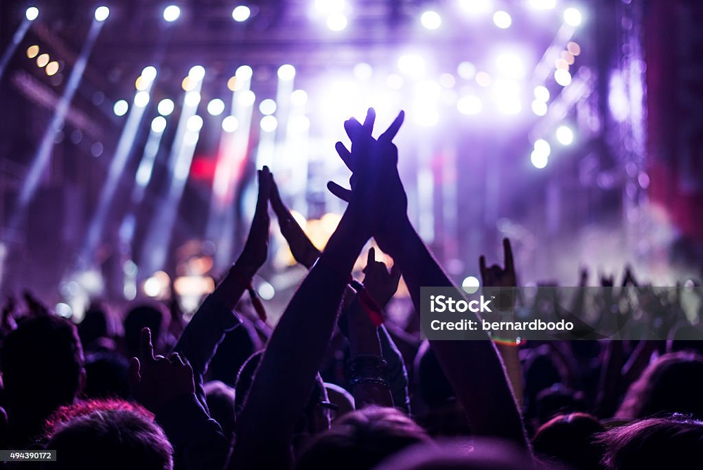 This party's on fire Audience with hands raised at a music festival and lights streaming down from above the stage. Soft focus, blurred movement. Applauding Stock Photo