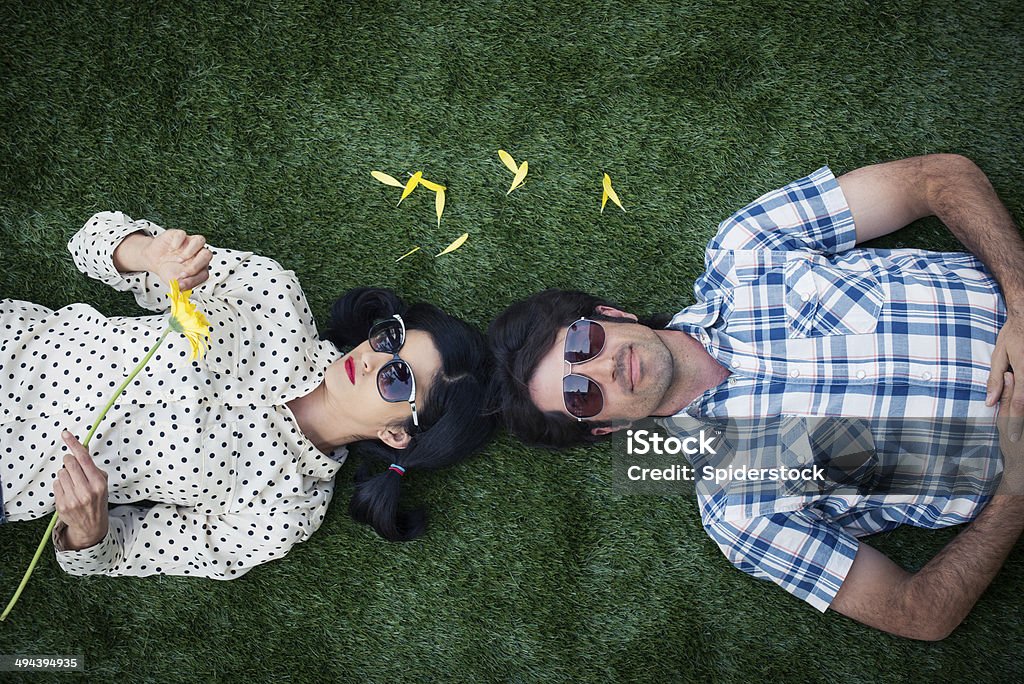 High Angle view Of Romantic Couple High angle view of a romantic hipster couple lying on grass. The woman is holding a yellow Gerber daisy. 30-39 Years Stock Photo