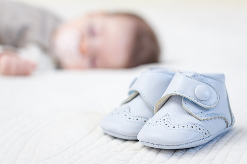 Closeup of baby blue leather shoes over a bed and adorable babe sleeping on the background