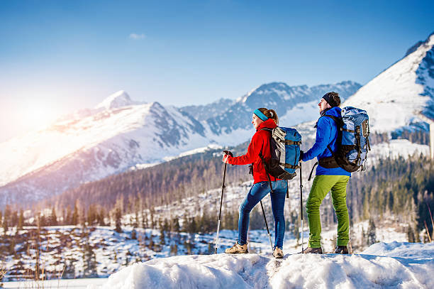 Young couple on a hike Young couple hiking outside in sunny winter mountains nordic walking pole stock pictures, royalty-free photos & images