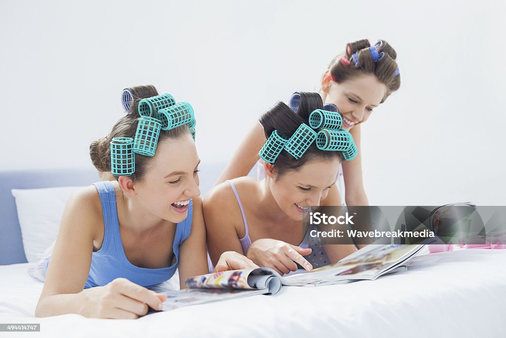 Girls wearing pajamas and hair rollers reading magazines Girls wearing pajamas and hair rollers sitting in bed with magazines at sleepover 18-19 Years Stock Photo