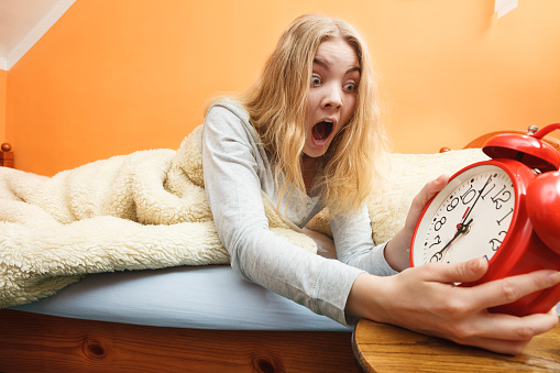 Panic woman waking up late in morning turning off alarm clock. Young girl laying in bed.