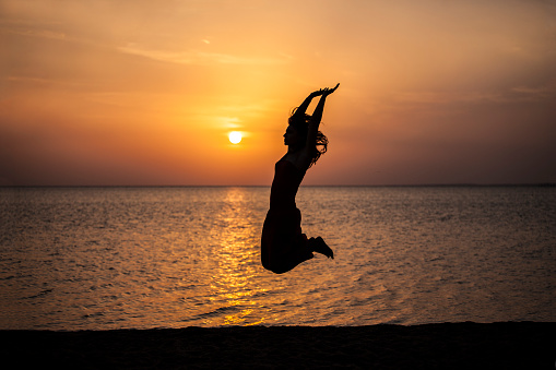 Woman jumping beautiful silhouette against the sea and dawn. Tourism, travel, movement, joy, sunset