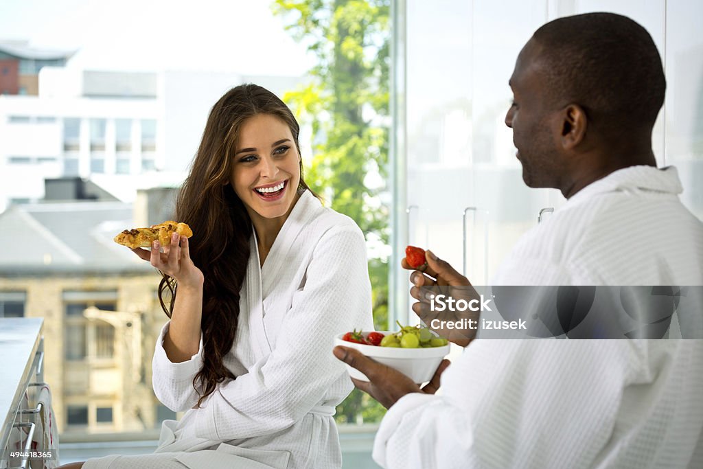 Happy morning Afro american man and beautiful brunette wearing white bathrobes sitting in the kitchen in the morning and having breakfast. Morning Stock Photo