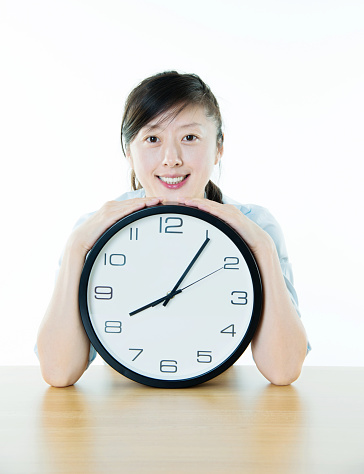 Young woman holding a wall clock against white background.