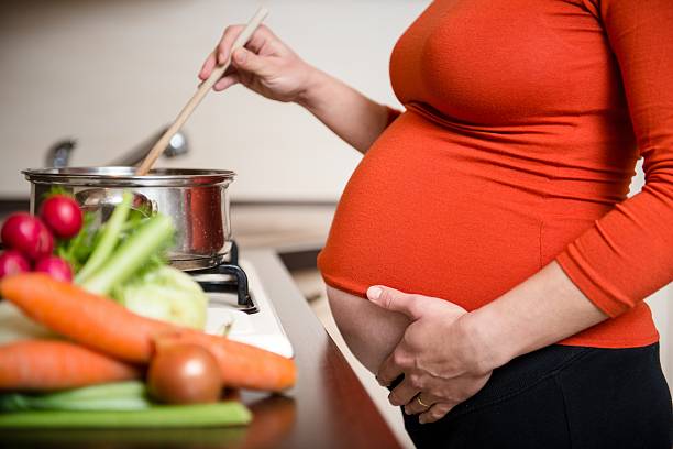 Pregnant woman cooking vegetables stock photo
