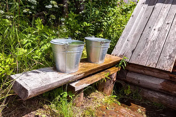 Metal buckets with cool water standing on a bench at the village water well