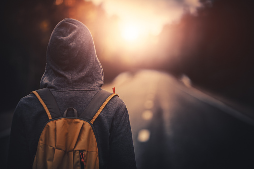 Traveler with backpack walking forward alone at sunset. Stock photo.