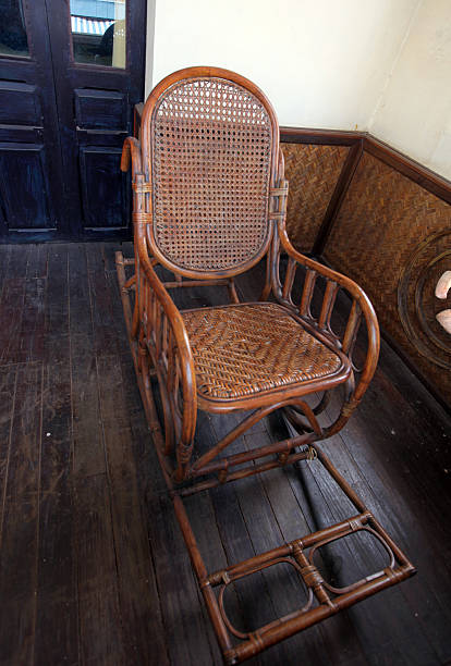 Rocking wood chair alone in the middle of a balcony outside with bushes at the background