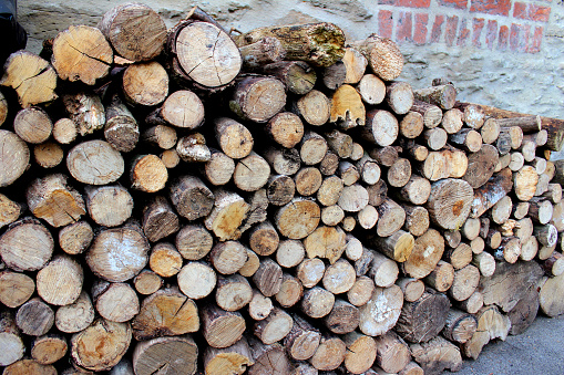 Photo showing a large pile of chopped logs against a sheltered brick wall, drying out ready for the wood burner in the cold English winter months.