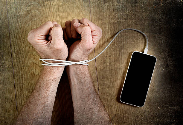 man hand wrists wrapped  with mobile phone cable handcuffed stock photo
