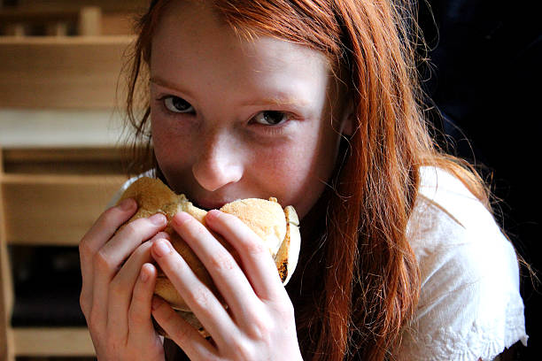 istock Young girl eating a cheese burger / beef burger in bap 494437669