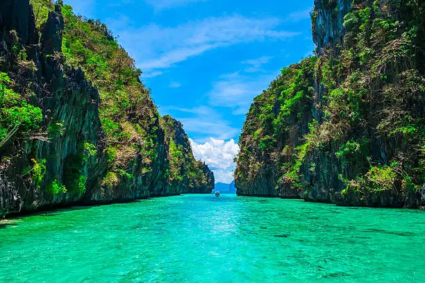 Tropical landscape with rock islands, lonely boat and crystal clear water, El Nido, Palawan, Philippines