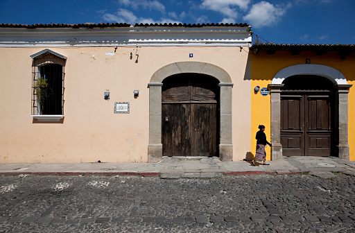Antigua, Guatemala -- November 25, 2010: Woman is walking along empty street with colorful colonial style houses