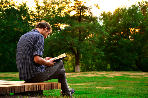 Guy sitting on a bench in the park reading book