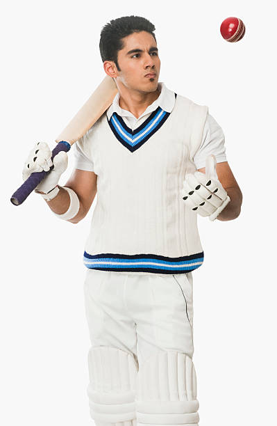 Cricket batsman holding a bat and looking at a ball