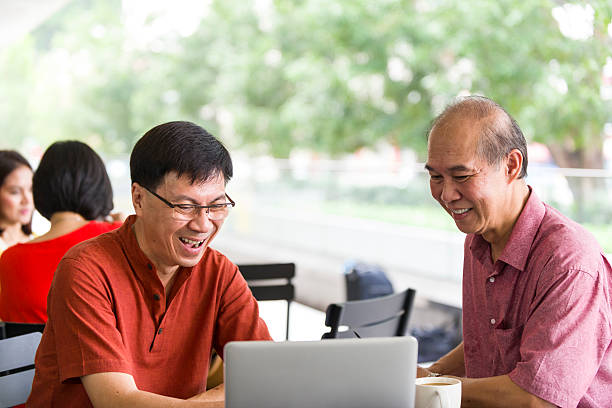 Two Mature Men Using Notebook at Outdoor Cafe stock photo