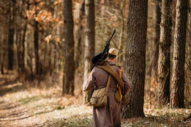 Young unidentified re-enactor dressed as Soviet soldier machine gunner goes along a forest road.