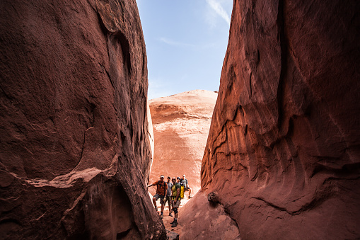 five men stand at the base of a slot canyon with sandstone walls and a clear blue sky beyond.  such adventure opportunities can be found in the slot canyons of the escalante.  horizontal wide angle composition.  