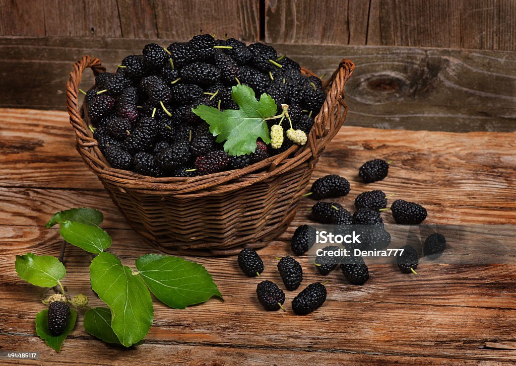 Mulberries with leaves on a wicker basket basket  with black mulberries on  wooden background Basket Stock Photo