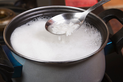 Close-up of a spatula over a pan of rice boiling on a stove