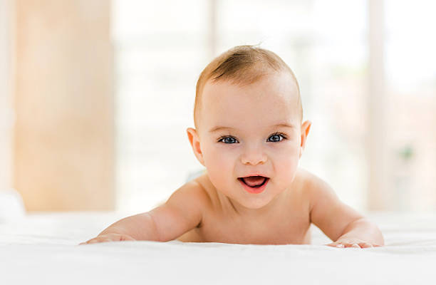 Cute baby in bed smiling and looking at camera. Portrait of happy baby boy lying down in bed and looking at camera. 8 weeks stock pictures, royalty-free photos & images