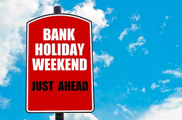 Bank Holiday Weekend Just Ahead motivational quote written on red road sign isolated over clear blue sky background. Concept  image with available copy space